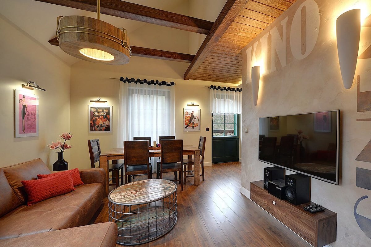 A modern living room with a wooden ceiling, a dining area with a table and chairs, a sofa, and a TV mounted on the wall.