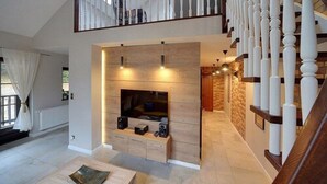 Un vaste espace de vie doté d’un téléviseur encastré, de meubles en bois et d’un escalier avec des balustrades blanches.