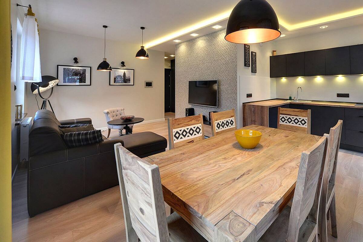 A modern kitchen with dark cabinets, a wooden dining table, and pendant lighting.