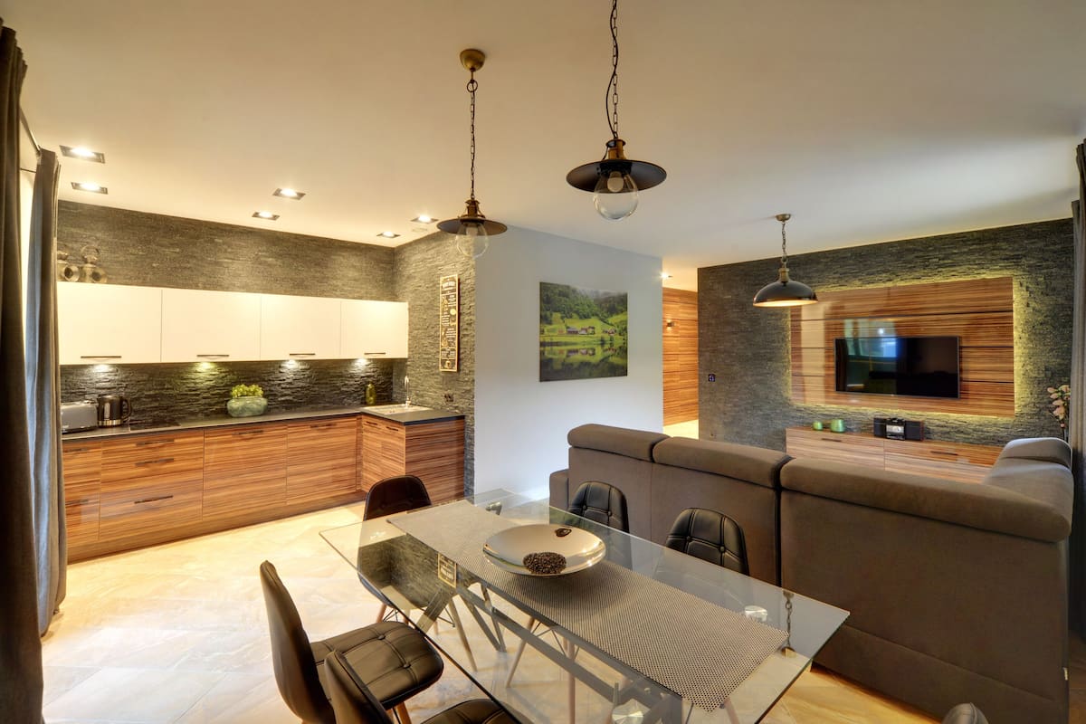 A modern kitchen with wooden cabinets, a dining table with chairs, and a built-in TV.