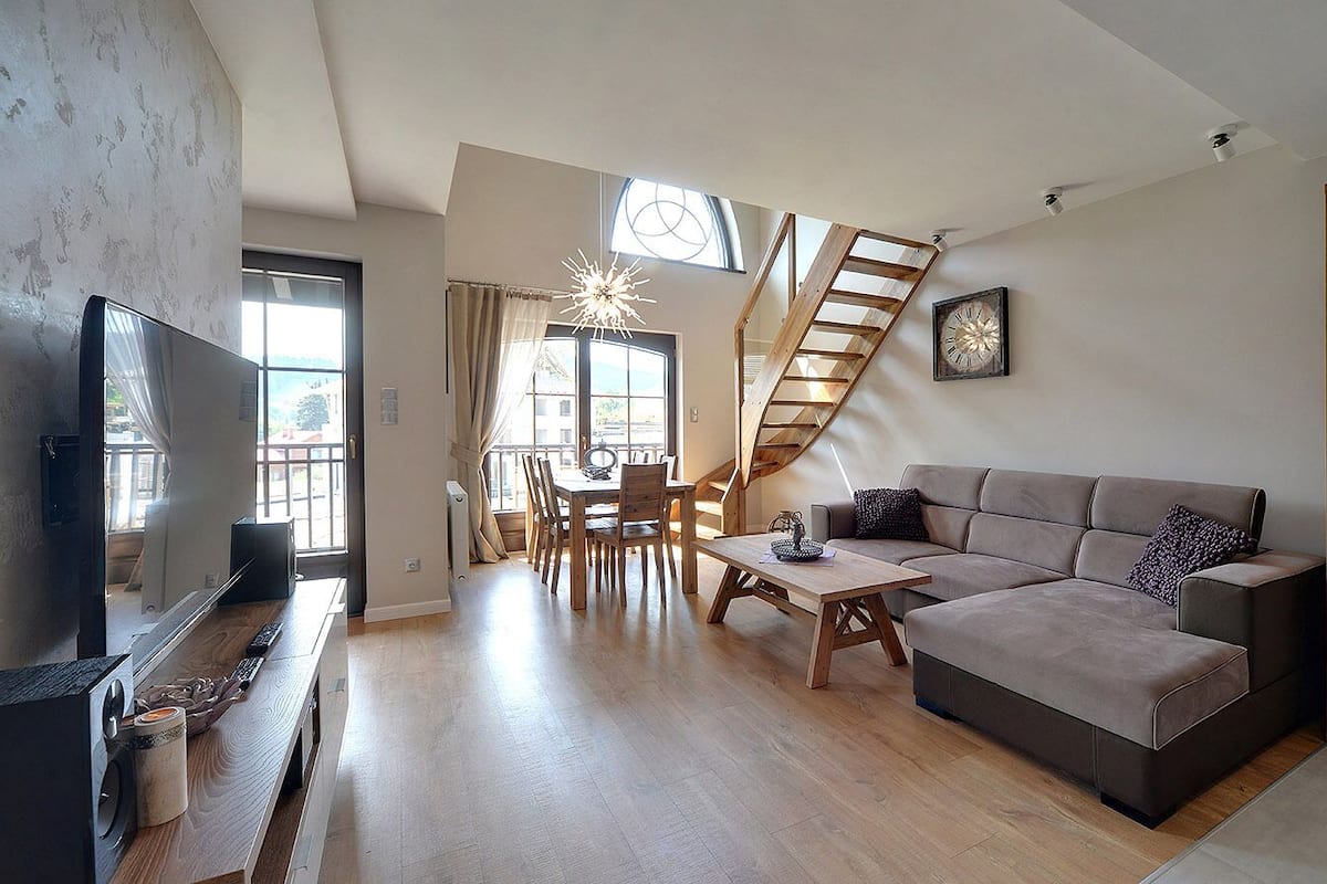 A spacious living area with a wooden dining table, a sofa, a TV, and a staircase.