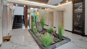 Un hall d’entrée spacieux avec un sol en marbre, un grand bac à plantes orné de verdure, un escalier et un lustre moderne.