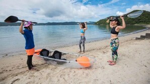 Three people on a beach with kayaks and a paddleboard, a clear sky, and a calm sea. - Zerogravity koniya clubhouse (Setouchi)