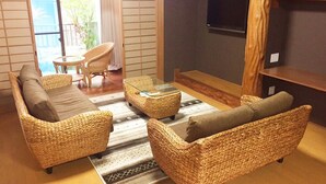 A cozy living area with wicker furniture, a glass coffee table, and a flat-screen TV mounted on the wall. - Zerogravity koniya clubhouse (Setouchi)