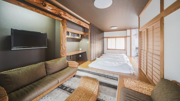 A traditional Japanese-style room with tatami flooring, a low wooden ceiling, a television mounted on the wall, and a sliding door. - Zerogravity koniya clubhouse (Setouchi)