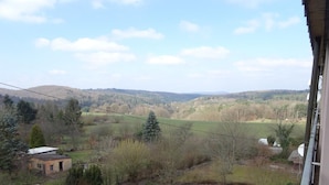 Blick aus einem Fenster auf eine ländliche Landschaft mit Feldern, Bäumen und einer entfernten Hügelkette.