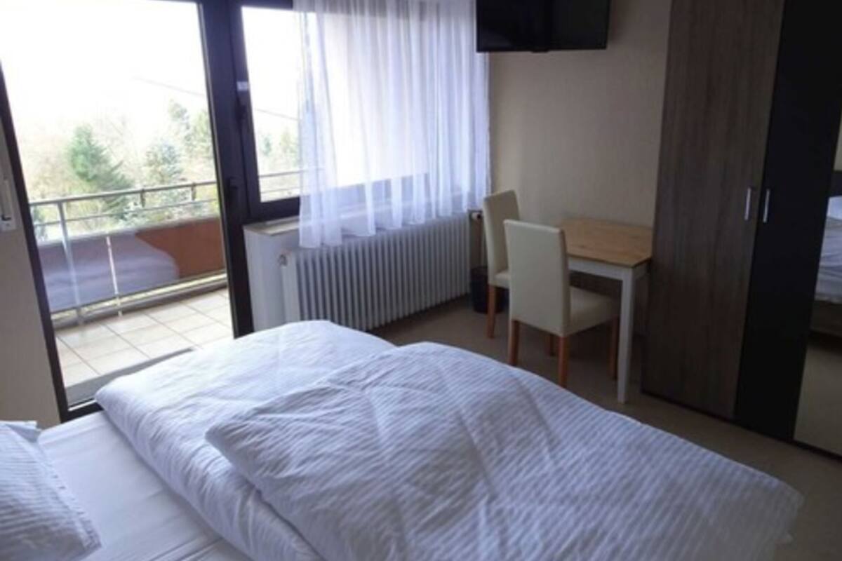 Een hotelkamer met een bed, bureau, stoel, kledingkast en een televisie aan de muur.