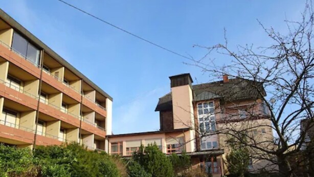 Ein mehrstöckiges Gebäude mit Balkonen, einem Gartenbereich und einer Mischung aus moderner und traditioneller Architektur.