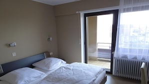 Ein Hotelzimmer mit Bett, einem Fenster mit Blick und einer Tür, die auf einen Balkon führt.