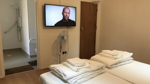 A hotel room with a bed, a TV mounted on the wall, a fan, and a shower area. - Oxford Bed and Breakfast (Kidlington)