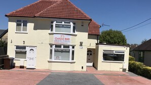A two-story building with a sign for Oxford B&B, featuring a tiled roof, a paved entrance, and a small side entrance. - Oxford Bed and Breakfast (Kidlington)