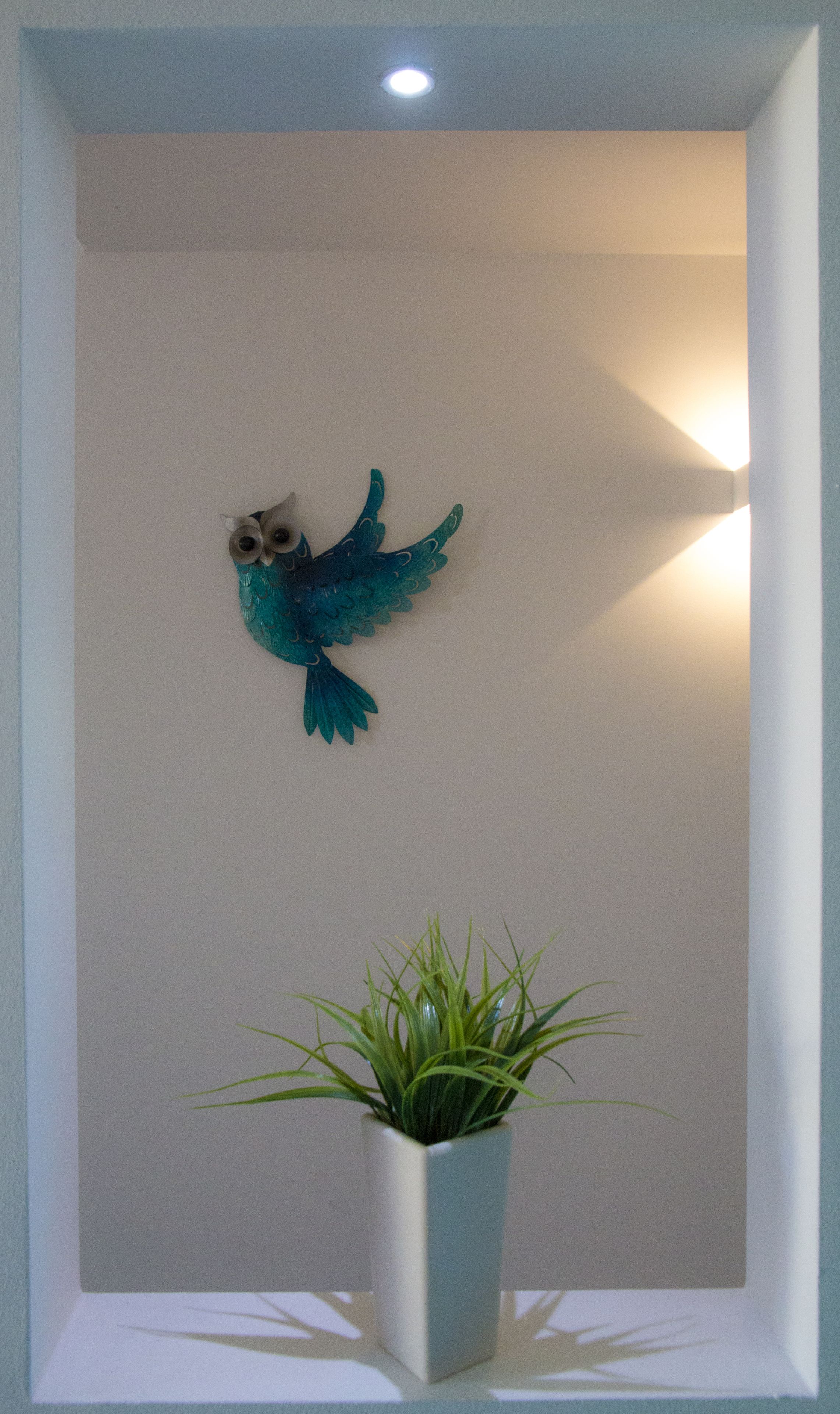 A framed wall decoration of a blue bird and a potted plant.