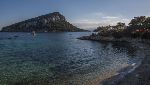 A coastal scene with a rocky island, clear water, and boats. - Hotel Maria (Golfo Aranci)