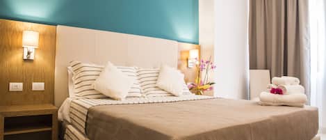 Habitación de hotel con una cama grande, una mesita de noche, una lámpara, un florero con flores y una silla con toallas.
