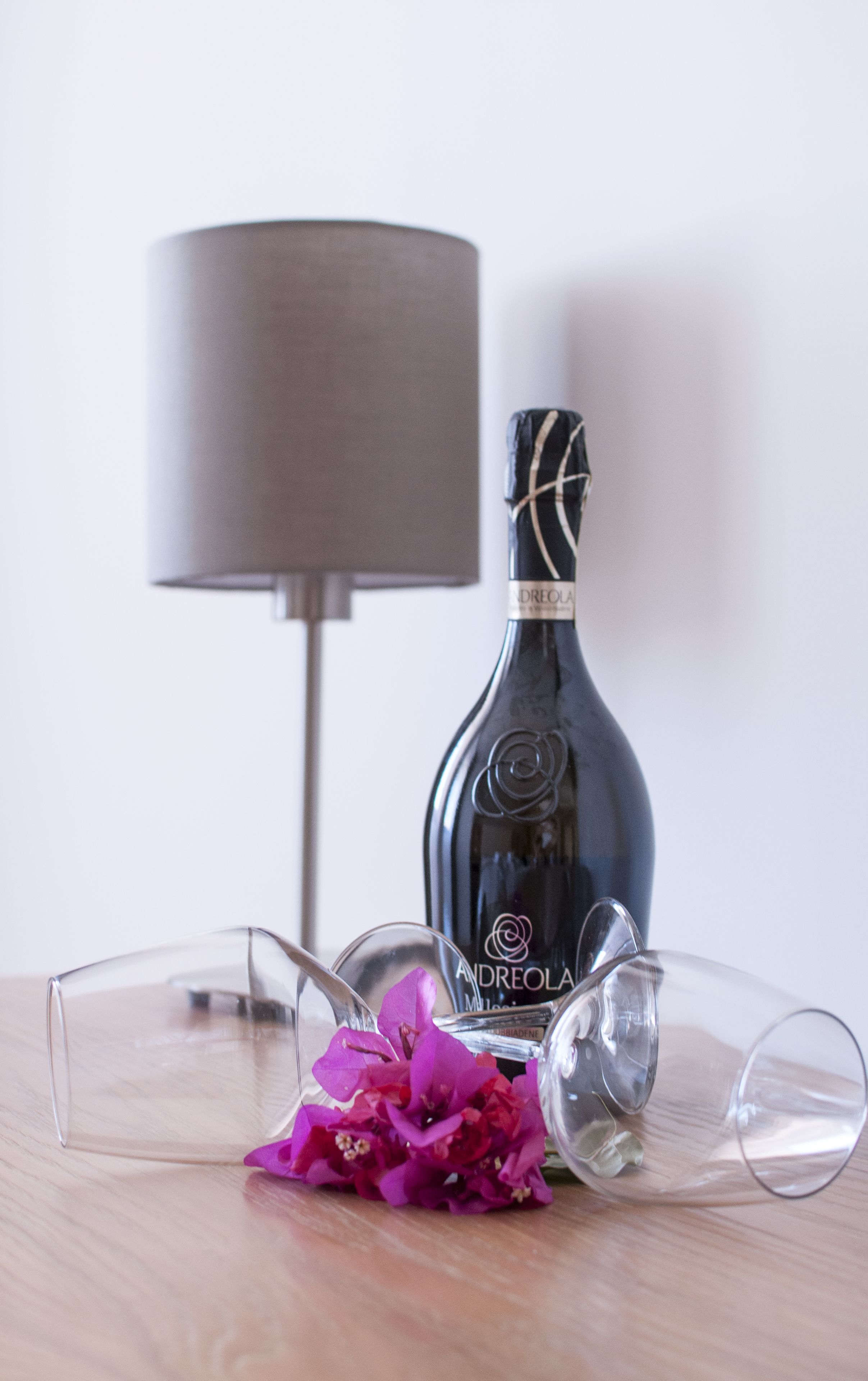 En flaske vin, et glas og en blomst på et bord, med en lampe i baggrunden.
