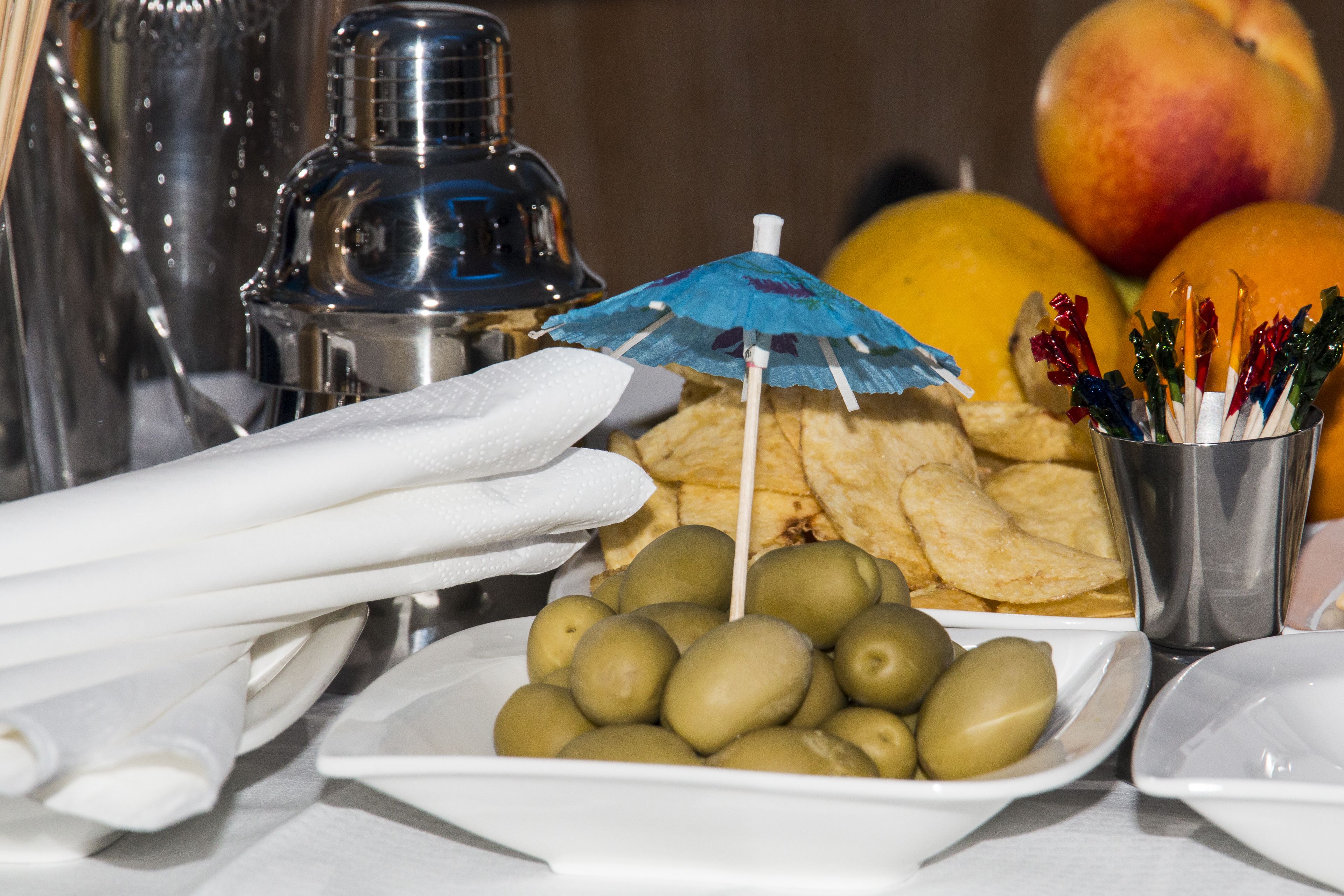 A table with olives, chips, a small umbrella, and a container with toothpicks.