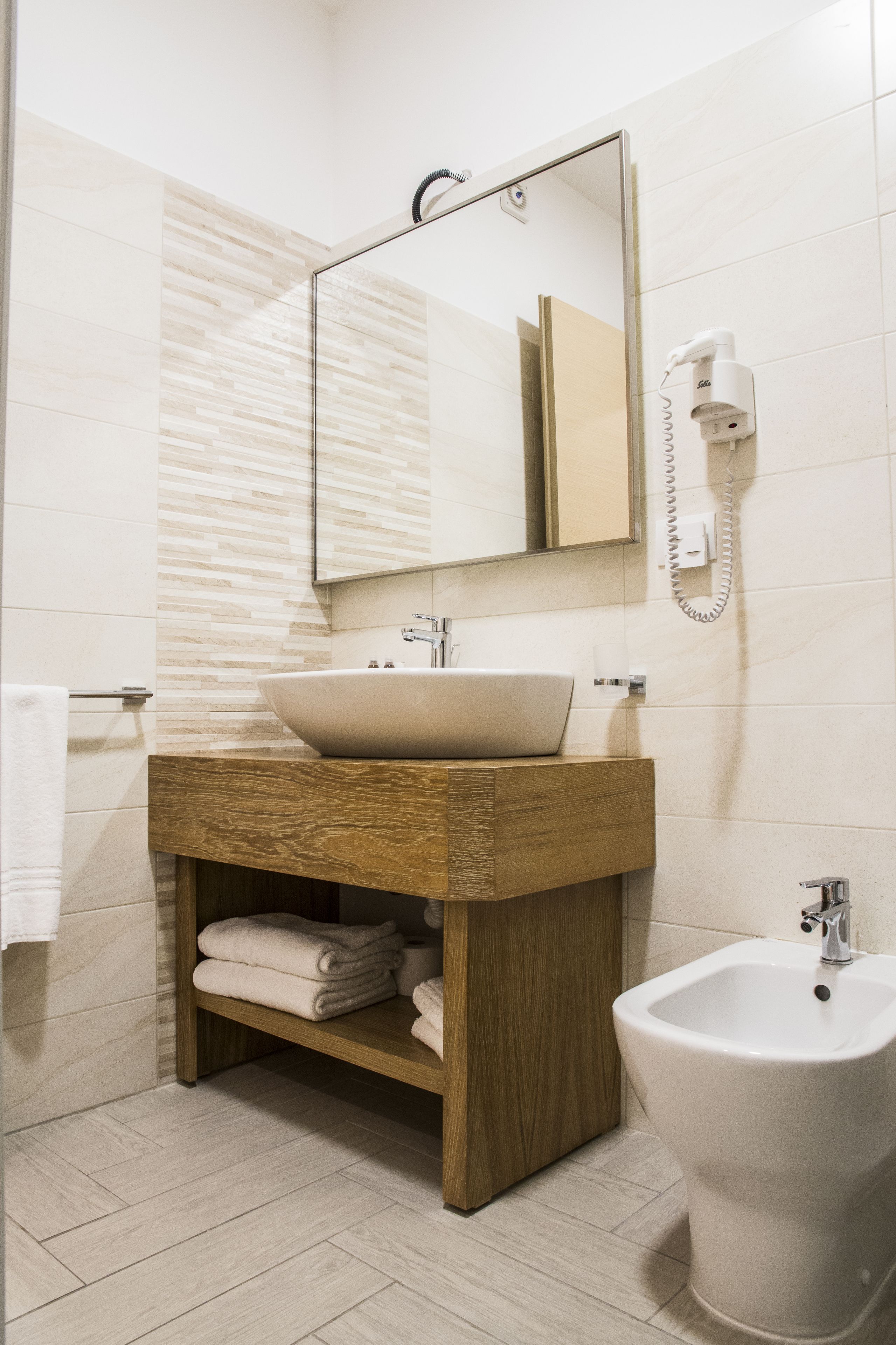 A modern bathroom with a wooden vanity, a large mirror, a bidet, and a towel rack.