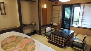 A traditional Japanese-style room with tatami flooring, a low table with a checkered table runner, a bed with a floral-patterned blanket, and sliding doors with a view of greenery outside. - Hananoyado Fukuya (Hakone)