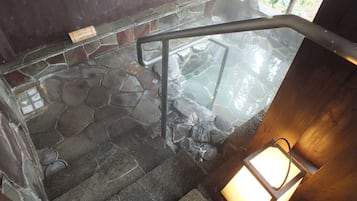 A stone staircase leading to a hot spring area with a wooden railing and a stone wall.