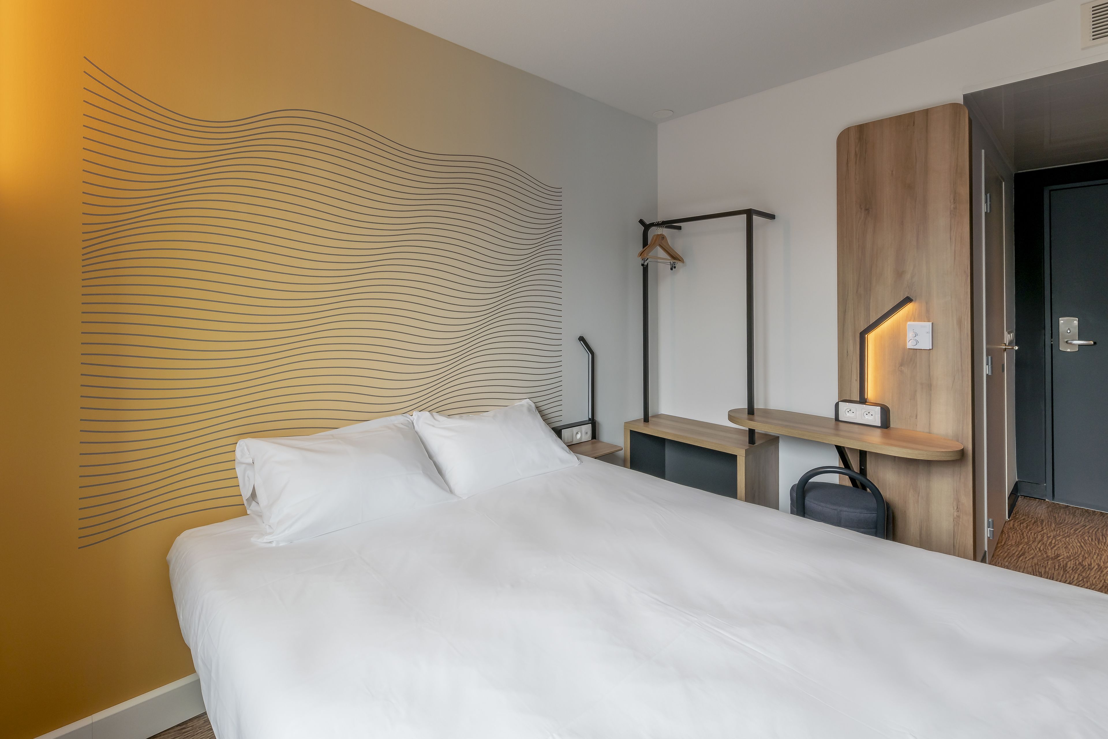 Een moderne hotelkamer met een groot bed, een houten hoofdbord, een nachtkastje met een lamp en een kledingkast.
