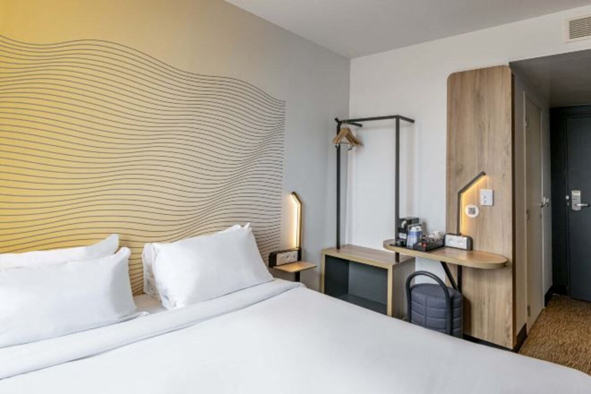 A hotel room with a bed, bedside tables, a desk, a lamp, and a wardrobe.
