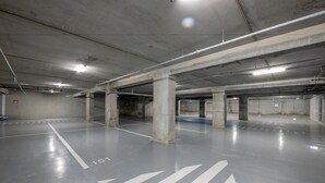 An empty parking garage with concrete pillars, marked parking spaces, and overhead lighting.