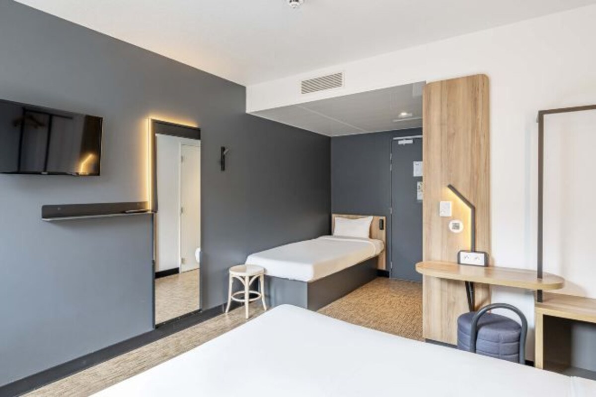 A modern hotel room with a large bed, a desk, a chair, and a small stool.