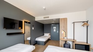 A hotel room with two single beds, a TV, a mirror, a desk with a chair, and a coat rack.
