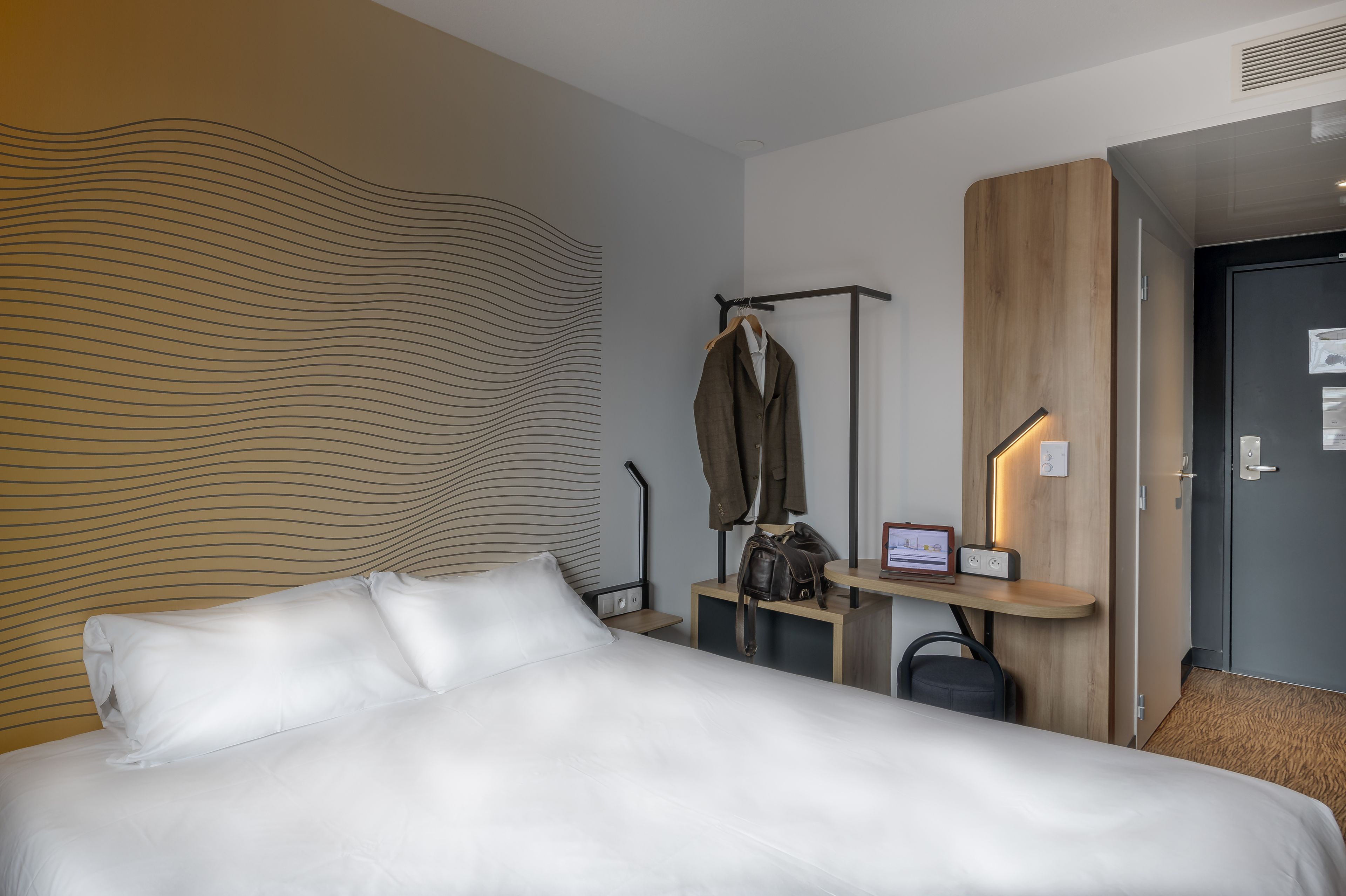 Una habitación de hotel con una cama grande, un escritorio con silla, un perchero y una puerta.