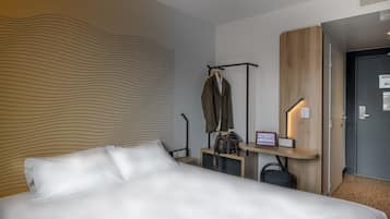 Una habitación de hotel con una cama grande, un escritorio con silla, un perchero y una puerta.
