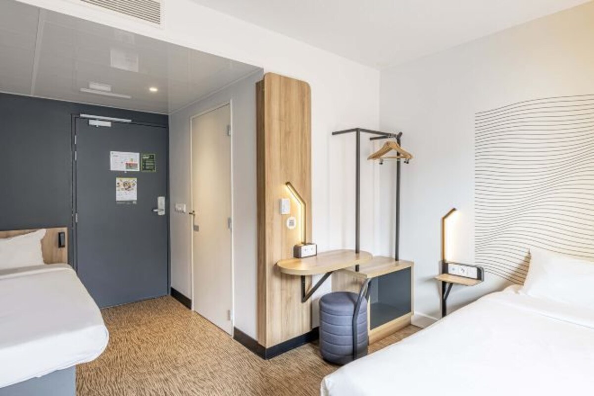 A hotel room with a bed, a desk with a chair, a wardrobe, and a coat rack.
