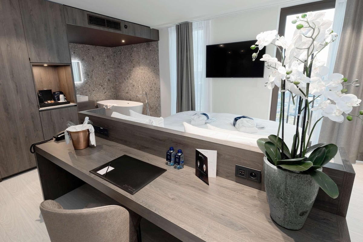 A modern bathroom with a large bathtub, a vanity with a sink, a mirror, and a potted orchid.