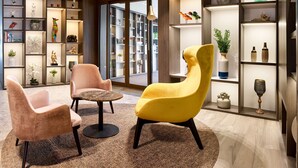A modern living room with two armchairs, a coffee table, and a bookshelf filled with decorative items. - Radisson Blu Hotel Bruges (Bruges)