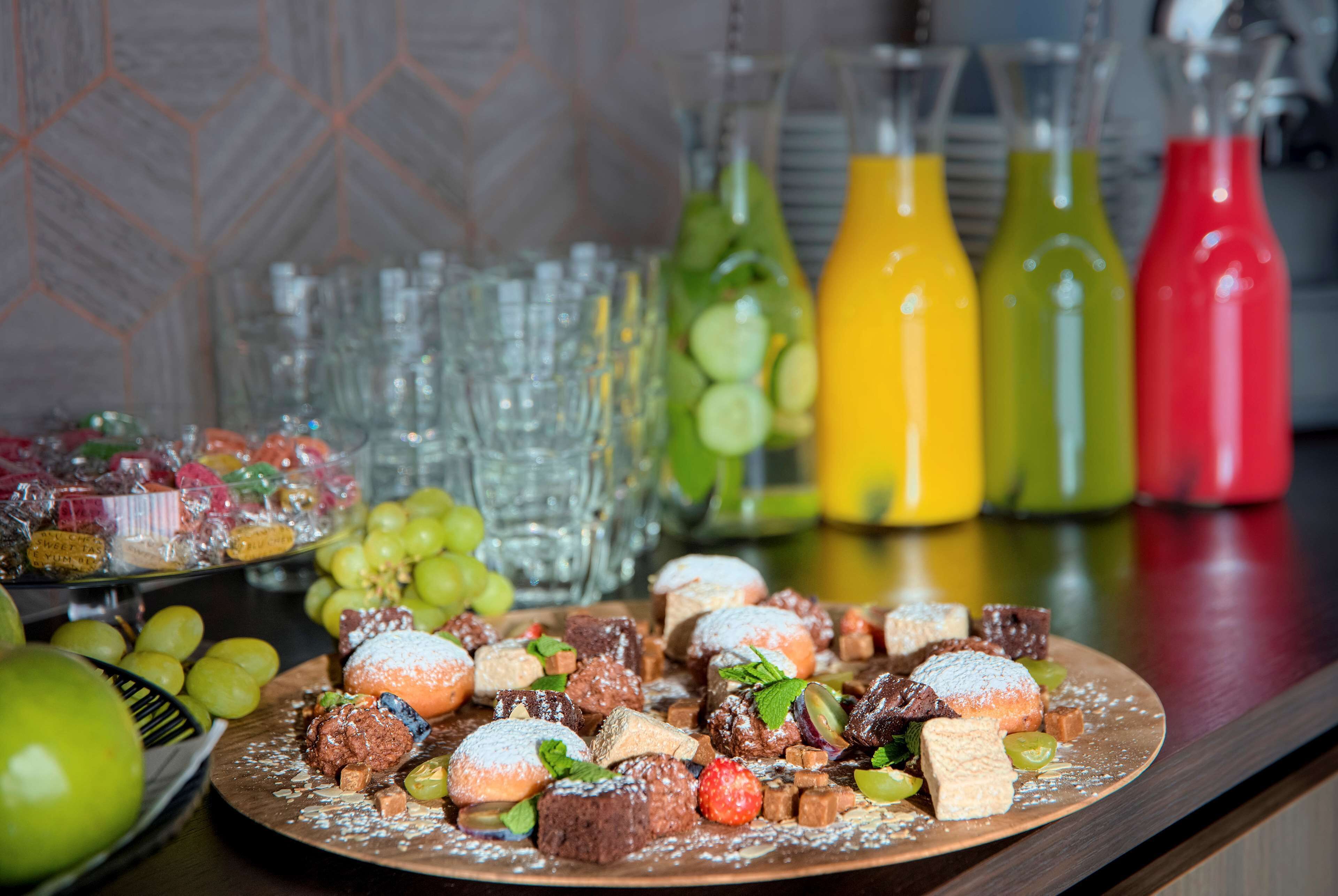 Un plato de postres con diversos dulces y frutas, rodeado de botellas coloridas y vasos transparentes.