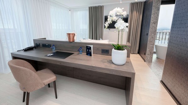 A modern hotel room with a large desk, a chair, a potted plant, and a view of the city. - Radisson Blu Hotel Bruges (Bruges)