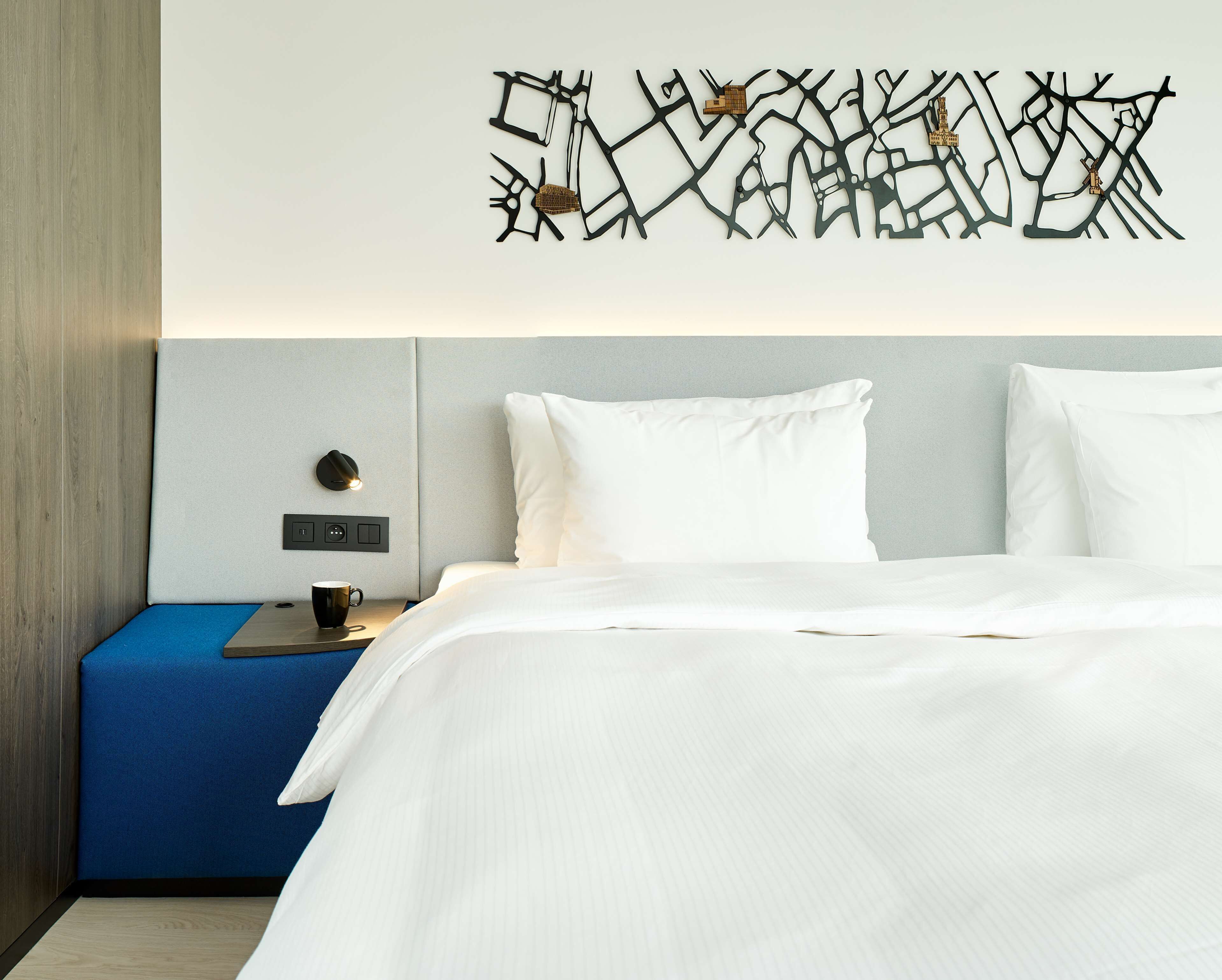 A hotel room with a bed, a nightstand, a wall-mounted lamp, and a decorative wall piece.
