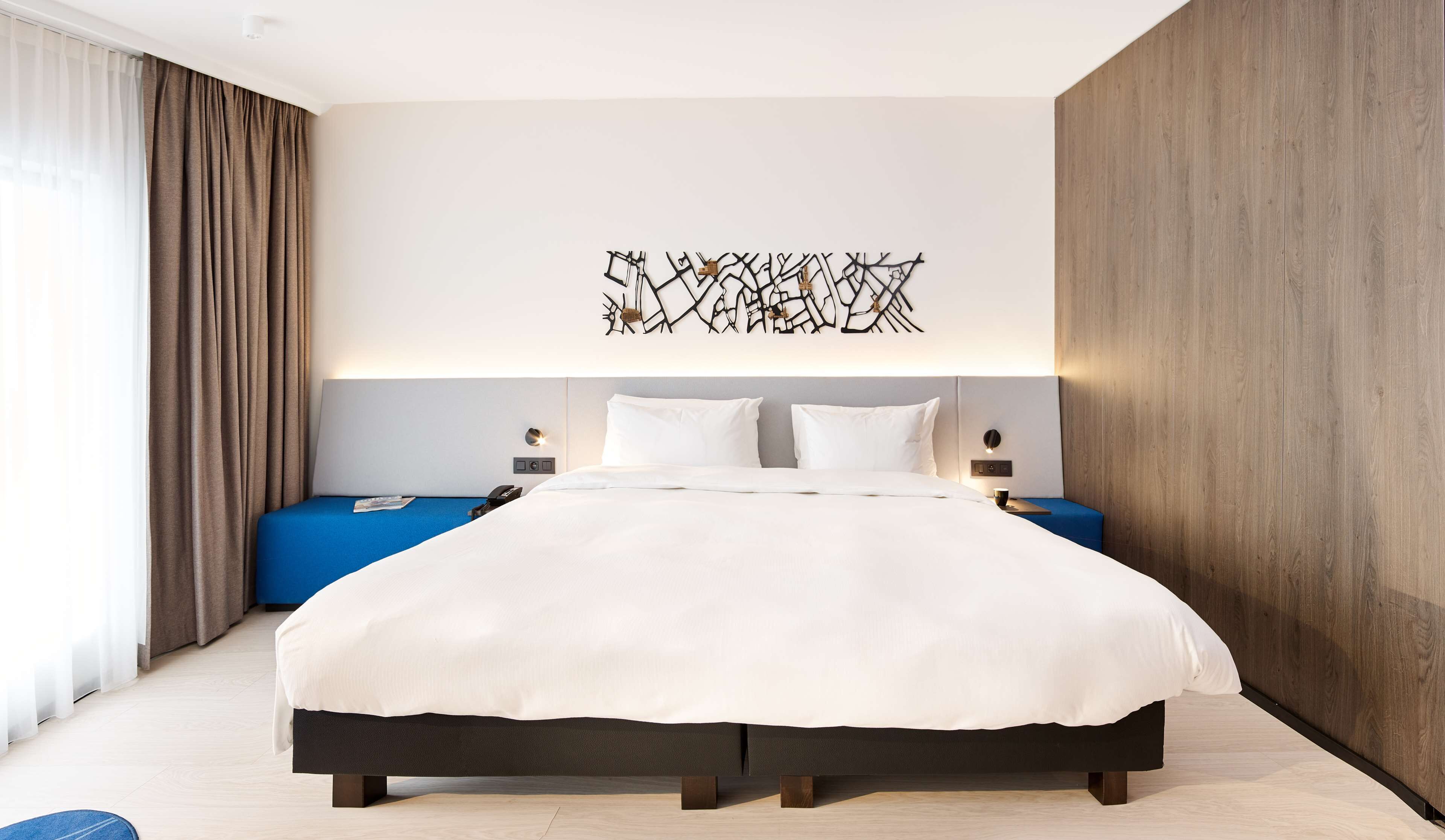 Ein modernes Hotelzimmer mit einem großen Bett, einer blauen Akzentwand und einem dekorativen Kunstwerk darüber.