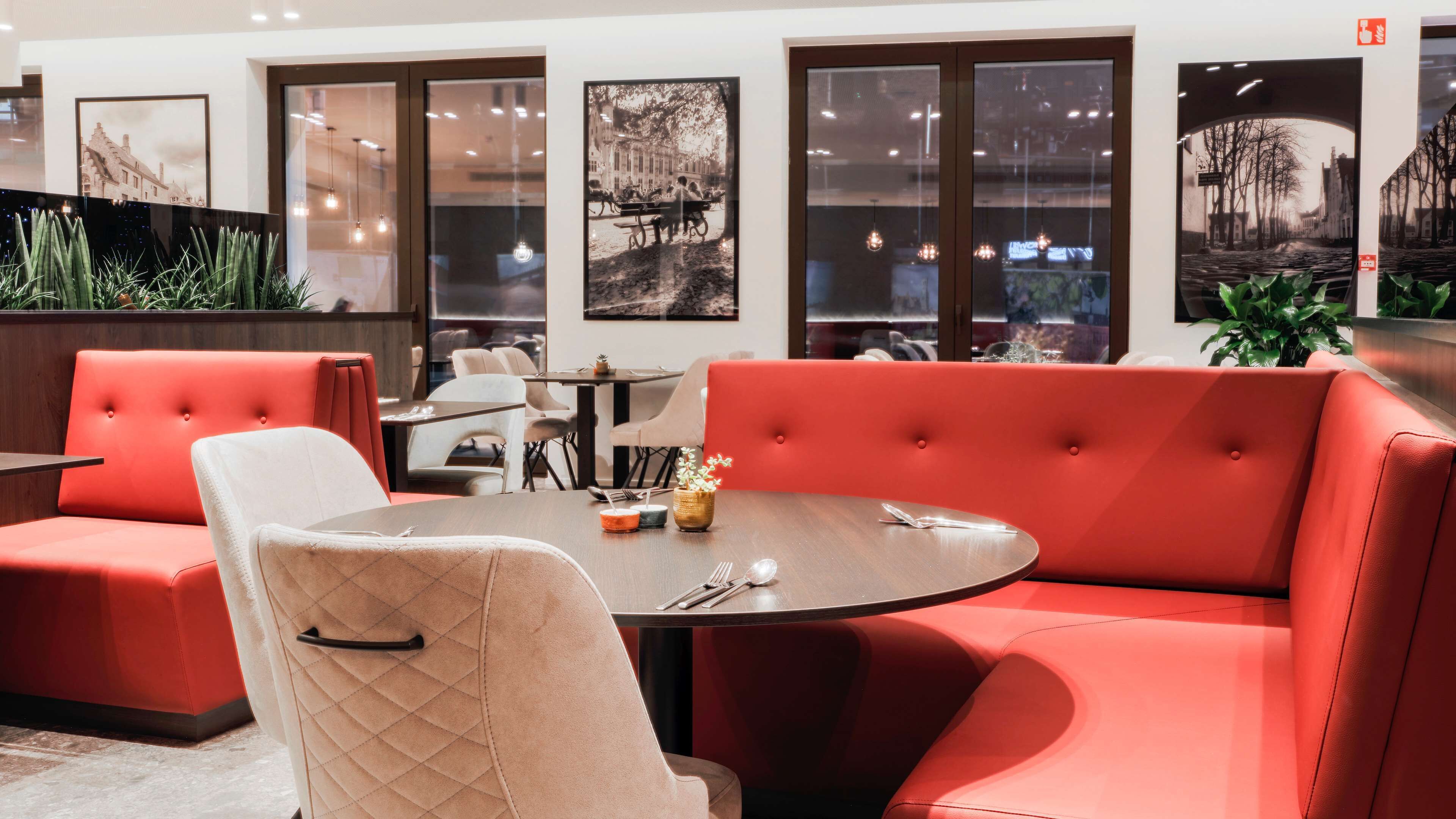A modern restaurant interior with red upholstered booths, a round table, and black-topped chairs.