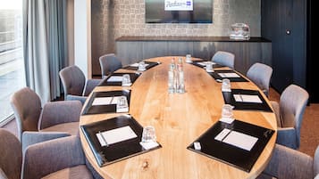 A conference room with a round wooden table, grey upholstered chairs, and a flat-screen TV on the wall displaying the Radisson Blu Hotel logo.