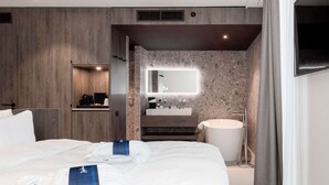 A modern hotel room with a large bed, a built-in vanity with a mirror, a bathtub, and a wooden panel wall. - Radisson Blu Hotel Bruges (Bruges)
