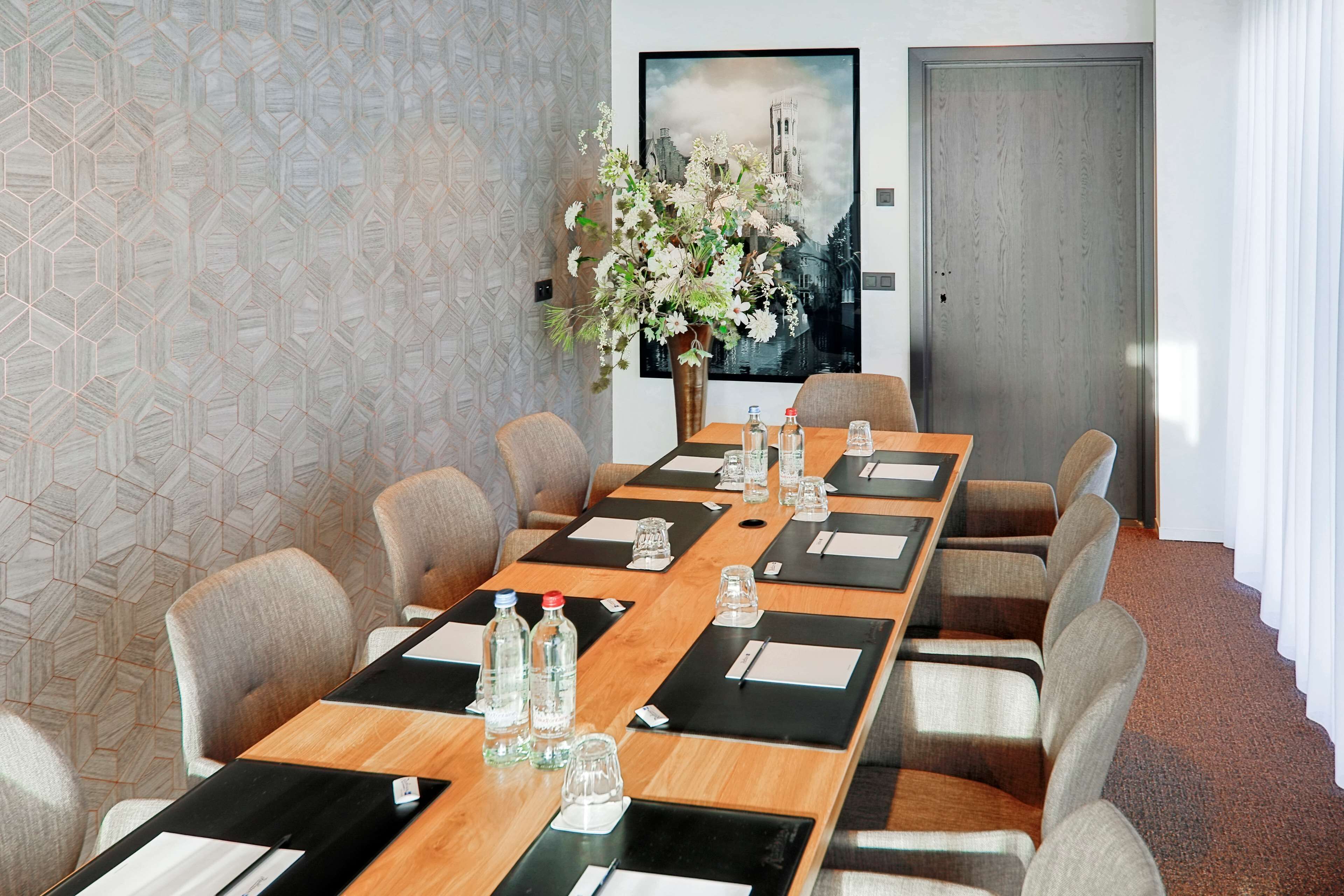 A conference room with a long table, multiple chairs, water bottles, and a vase with flowers.