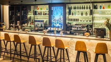 Zona de bar con mostrador de mármol, varios taburetes y estantes llenos de botellas y vasos.