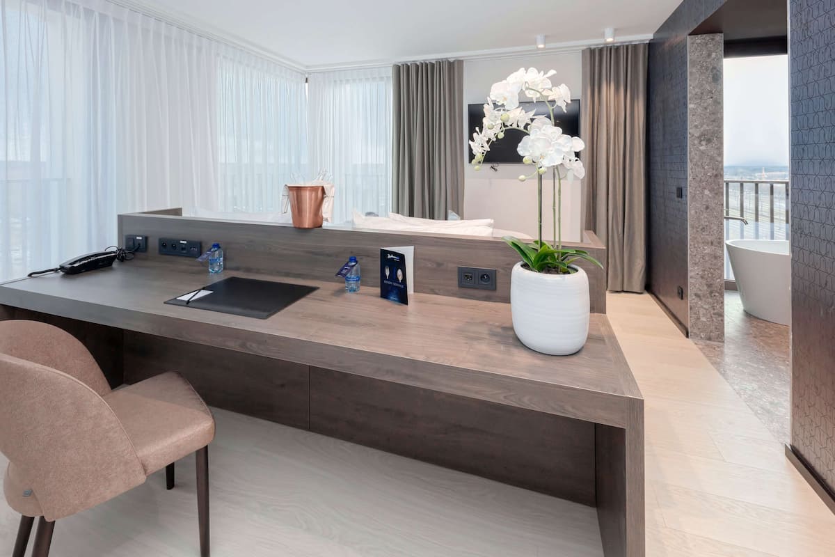 A modern hotel room with a large wooden desk, a chair, a potted orchid, and a bathtub.