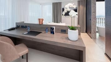 A modern hotel room with a large wooden desk, a chair, a potted orchid, and a bathtub.