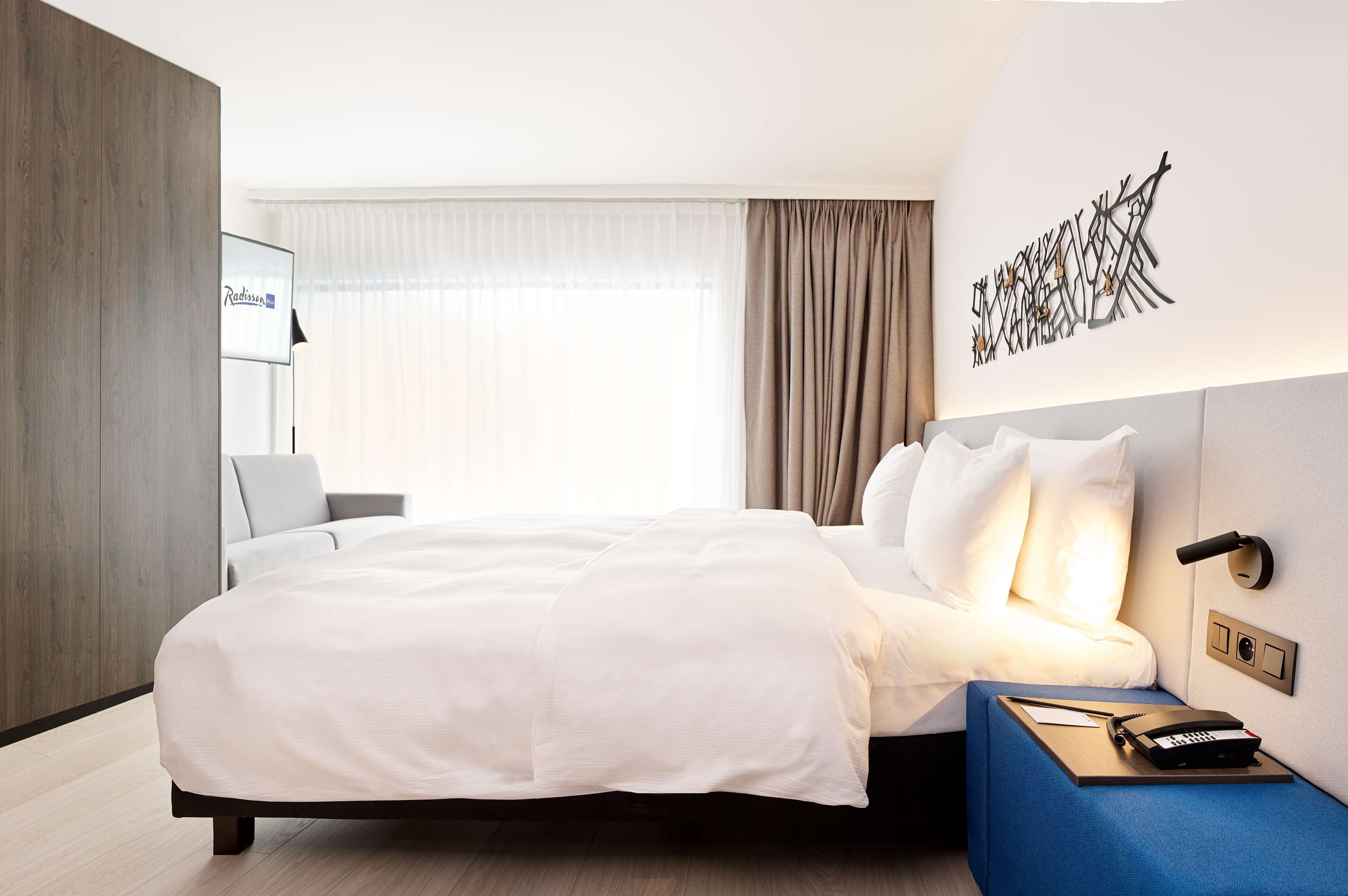 Et moderne hotelværelse med en stor seng, et natbord med telefon og en vægmonteret lampe.
