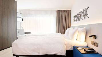 Et moderne hotelværelse med en stor seng, et natbord med telefon og en vægmonteret lampe.