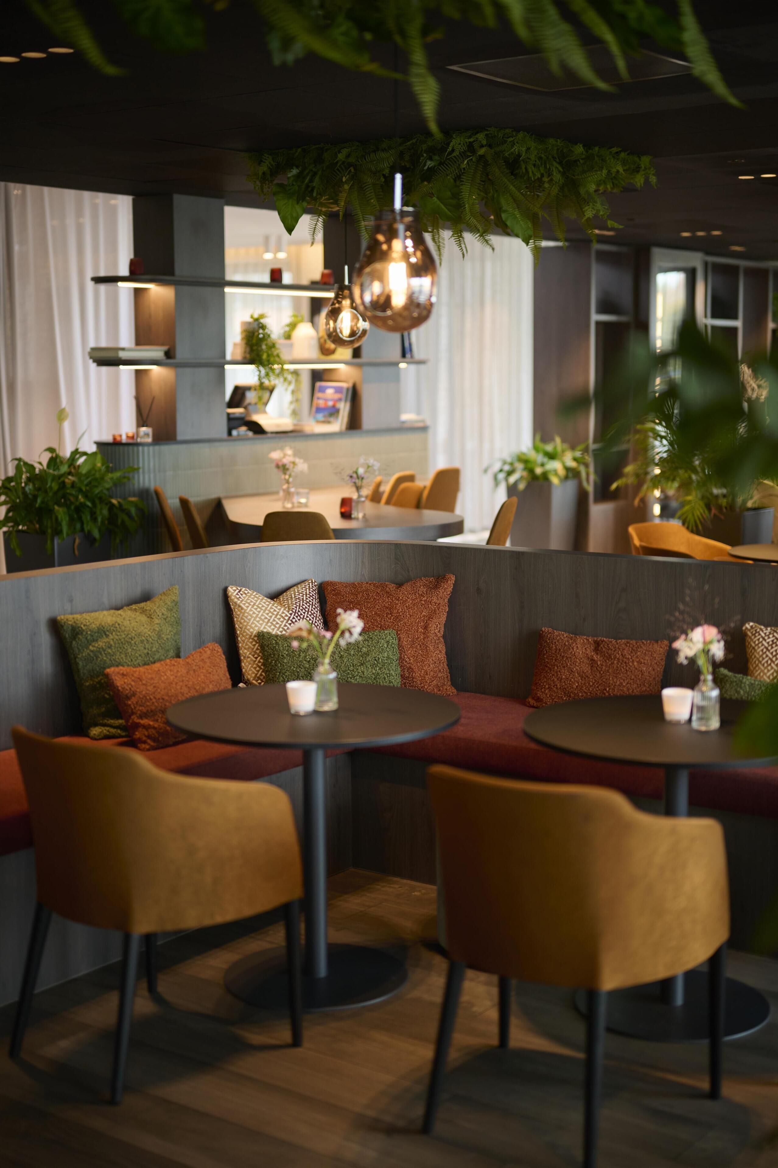 A modern restaurant with round tables, cushioned seating, and hanging plants.