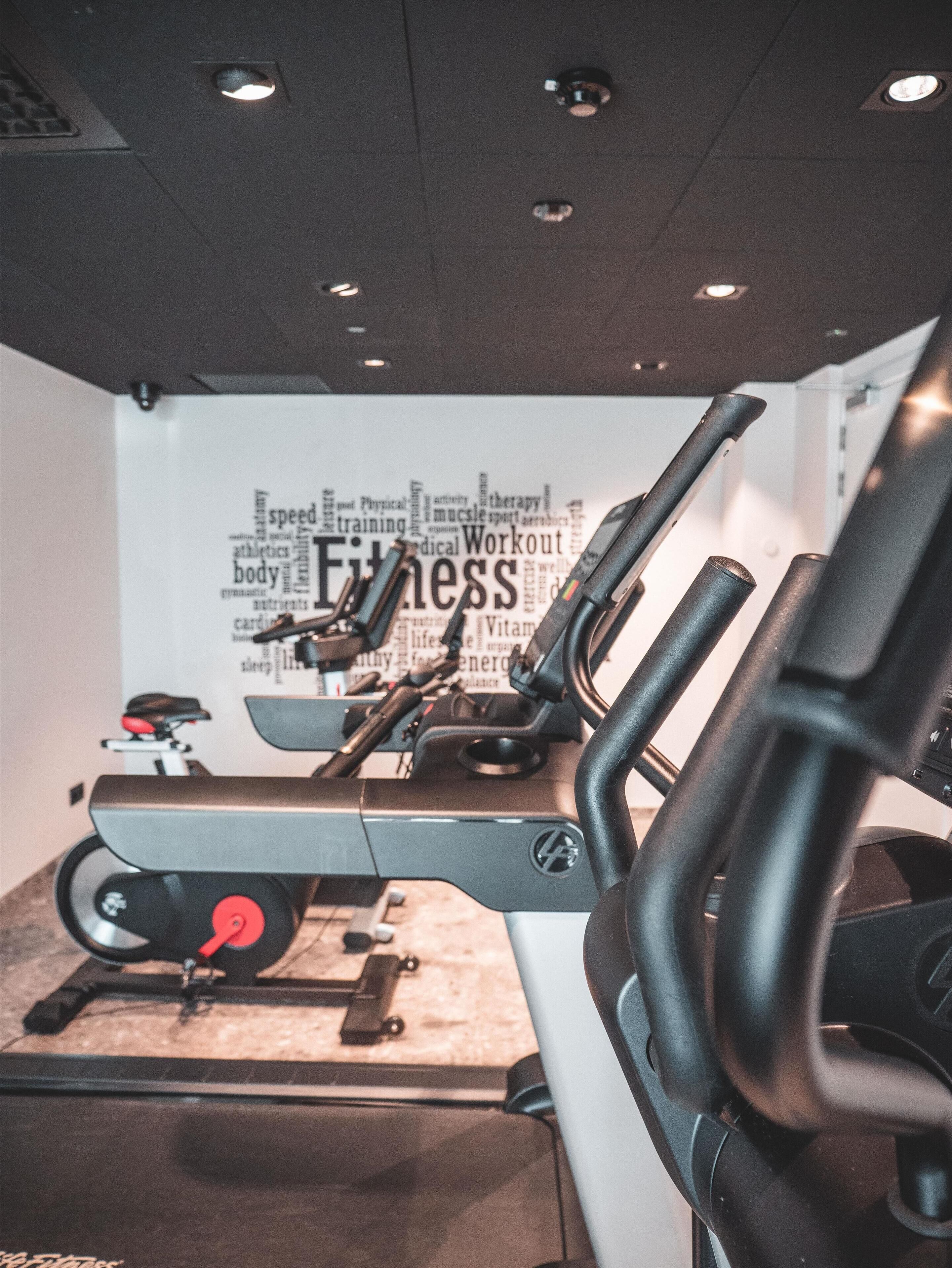 A gym with exercise equipment, a wall with fitness-related words, and a ceiling with lights.