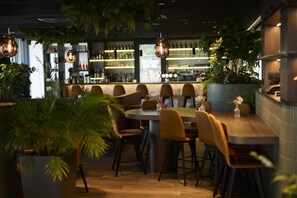 A restaurant with round tables, chairs, hanging lights, and potted plants. - Radisson Blu Hotel Bruges (Bruges)