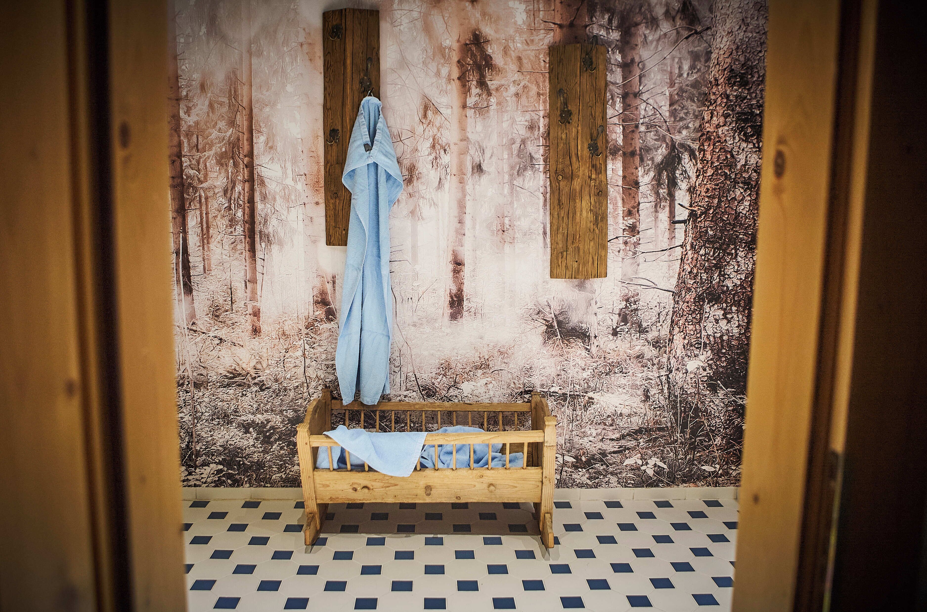 A room with a wooden bed, a blue towel, and a forest-themed wallpaper.